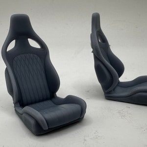 May include: Two gray racing car seats with a textured fabric design. The seats are made of a hard plastic material and have a sporty look.