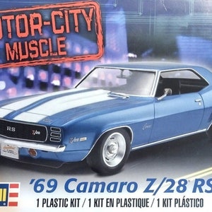 May include: A blue '69 Camaro Z/28 RS model car kit. The box features the text "MOTOR-CITY MUSCLE" and "Revell". The car has white racing stripes and chrome accents. The kit is 1:25 scale.