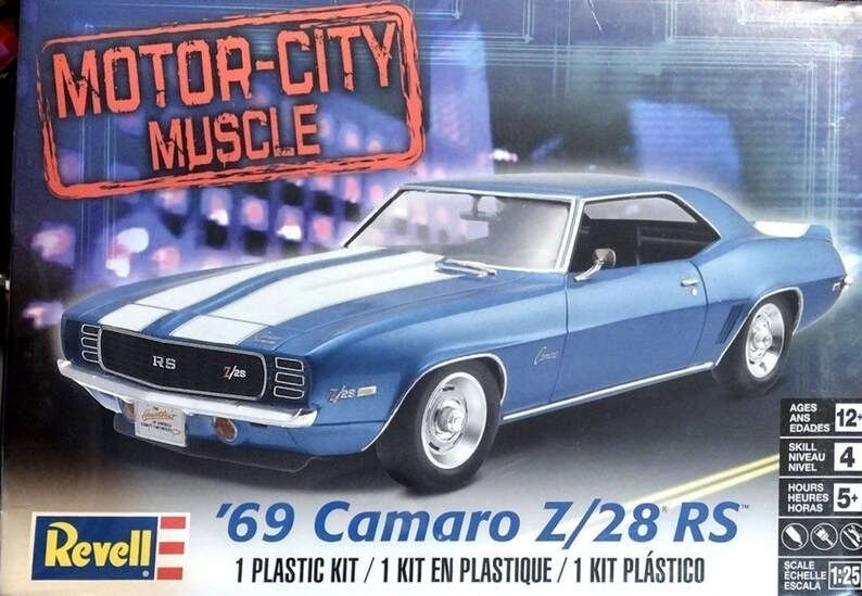 May include: A blue '69 Camaro Z/28 RS model car kit. The box features the text "MOTOR-CITY MUSCLE" and "Revell". The car has white racing stripes and chrome accents. The kit is 1:25 scale.