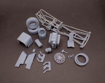 Op de afbeelding: Een modelkit van een dragsterauto, met verschillende onderdelen, waaronder het chassis, de motor, de wielen en de carrosseriedelen. De onderdelen zijn gemaakt van grijs plastic en zijn klaar om in elkaar te worden gezet.