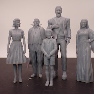 May include: A set of six grey 3D printed figurines depicting a family. The figures are of a man, a woman, a boy, a girl, a man in a suit, and a woman in a long dress.