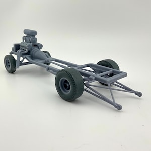 Peut inclure: Modèle gris d'une voiture de dragster. Le modèle présente un moteur détaillé, un châssis et quatre pneus gris foncé. Le dragster est conçu avec une carrosserie longue et profilée et un profil bas.