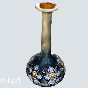 May include: A decorative, hand-painted ceramic vase with a bulbous base and a long, slender neck. The vase features a dark blue background with blue leaf and gold swirl designs. The top has a brown stopper.