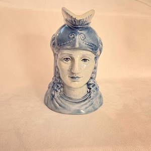 May include: A ceramic bust of a woman with blue and white coloring. The woman has curly hair and is wearing a helmet-like head covering. The bust is a decorative piece, likely for display.