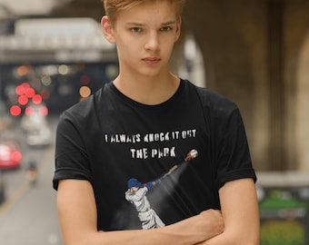 May include: Black t-shirt with the text "I ALWAYS KNOCK IT OUT THE PARK" above a baseball player illustration. The illustration shows a baseball player in a blue and white uniform hitting a baseball. The person in the image is wearing the t-shirt.