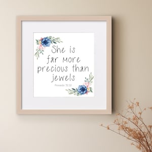 May include: Square framed print with the text "She is far more precious than jewels" and "Proverbs 31:10". The print is decorated with watercolor floral accents in blue, pink, and green. The frame is a light wood color.