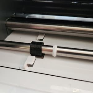 May include: Close-up of a silver metal rod with a black and white ring on it. The rod is part of a machine.