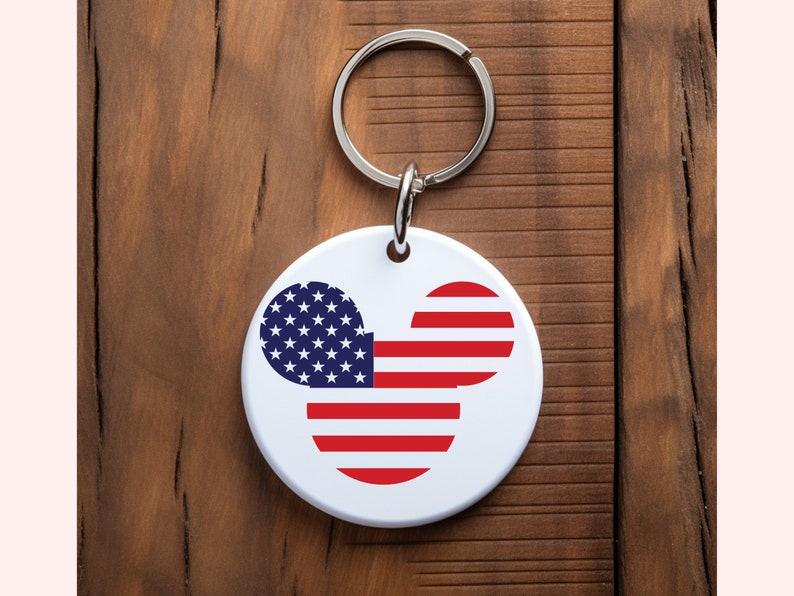 May include: A white round keychain with a red, white, and blue American flag design in the shape of Mickey Mouse's head.