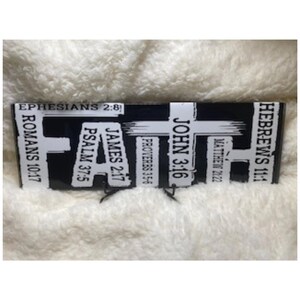 May include: A black and white rectangular sign with the word "FAITH" in large white letters. The sign features various Bible verses, including Ephesians 2:8, John 3:16, and Hebrews 11:1. The sign is set against a fluffy, white background.