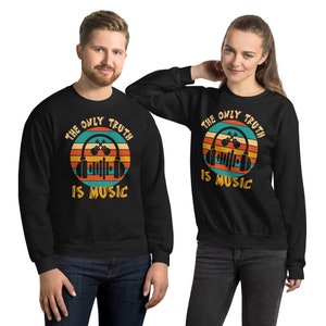 May include: Black sweatshirt with the slogan "THE ONLY TRUTH IS MUSIC" in a retro design. The graphic includes headphones, a musical staff, and a sunset-style background with orange, yellow, and teal stripes. The sweatshirt is worn by two people.