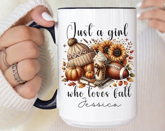 May include: White ceramic mug with a black handle. The mug features a graphic of a brown and white knit hat, a pumpkin, a football, a cup of coffee, and sunflowers. The text "Just a girl who loves fall Jessica" is printed on the mug.