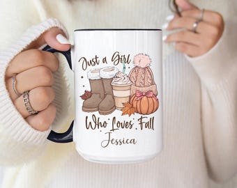 May include: White ceramic mug with a black rim and handle, featuring an illustration of fall-themed items. The design includes boots, a coffee drink, a hat, and a pumpkin. Text reads "Just a Girl Who Loves Fall Jessica."