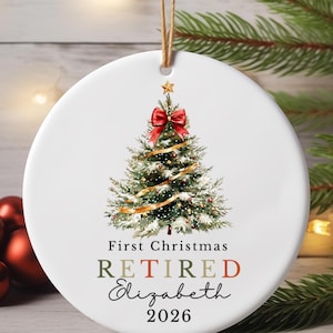 May include: A round white ceramic ornament featuring a watercolour illustration of a decorated Christmas tree with a red bow and gold ribbon. The text reads First Christmas RETIRED Elizabeth 2026 in black and muted red and green lettering.