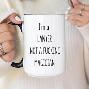 May include: White ceramic mug with a black handle and rim. The mug features the text "I'm a LAWYER NOT A FUCKING MAGICIAN" in black, bold font. A humorous gift for a solicitor.
