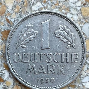 Può includere: Una moneta tedesca da 1 Deutsche Mark in argento del 1950. La moneta presenta un disegno a foglia di quercia su entrambi i lati del numero "1" e le parole "Deutsche Mark" sotto.