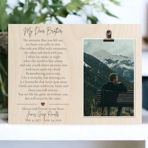 May include: A wooden photo frame with a clip at the top. The frame has a photo of a person sitting on a bench overlooking a mountain range. The frame has a poem about a brother printed on it. The poem reads "My Dear Brother. The moment that you left me, my heart was split in two. One side was filled with memories, the other side died with you. I often lay awake at night when the world is fast asleep, and take a walk down memory lane with tears upon my cheek. Remembering you is easy, I do it everyday, but missing you is a heartache that never goes away. I hold you close within my heart and there you will remain. You see life has gone on without you, but will never be the same. Always and forever in my heart James Grey Renaffs May 4, 1977 - June 24, 2023"