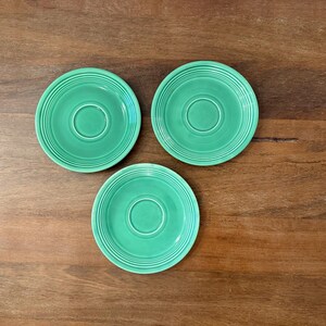 Puede incluir: Tres platillos de cerámica verde con un borde elevado y un pozo central. Los platillos están sobre una superficie de madera.