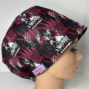 May include: A black and red surgical scrub cap featuring the text "A Nightmare on Elm Street" and images of Freddy Krueger. The cap has a repeating pattern of the movie title and imagery.