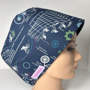 May include: A navy blue surgical scrub cap featuring a bicycle-themed design. The cap displays bicycle illustrations, gears, and a graph with text. The cap is made of fabric and is designed to cover the head.