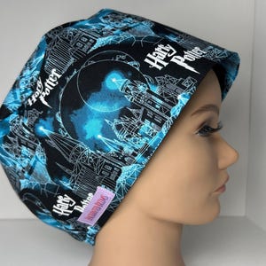 May include: A black and blue patterned scrub cap featuring a fantasy castle design with the words "Harry Potter". The cap is made of a soft fabric and has a tag that says "Enchanted Dreams".