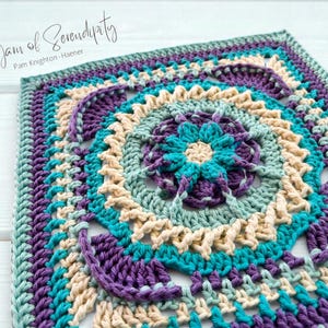 May include: A square, handmade crochet piece in shades of teal, purple, and cream. The design features a central floral motif surrounded by concentric circles and a scalloped border. The text "A Yarn of Serendipity" is in the upper left corner.