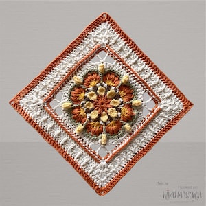 May include: A diamond-shaped crocheted doily. The central floral design uses orange, yellow, and green yarn, framed by a white and orange border. The text "Test by Hooked on Häkelmaschen" is visible. The overall design is intricate and detailed.