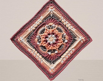 Könnte beinhalten: Ein quadratisches Häkelmotiv mit einem zentralen Blumenmuster in den Farben Burgunderrot, Dunkelgrau, Creme und Pfirsich. Das Design besteht aus komplexen Maschen in konzentrischen Schichten, die eine geometrische Form bilden, mit dem Text Test by Hooked on Häkelmaschen.