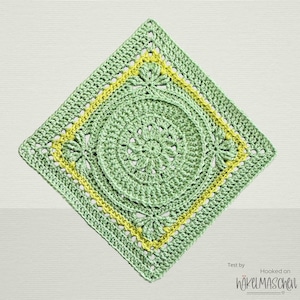 May include: A square, crocheted doily in shades of green and yellow. The center features a circular design, surrounded by a square border with floral accents. The doily is handmade, showcasing intricate stitch work. The text "Test by Hooked on Häkelmaschen" is in the bottom right corner.