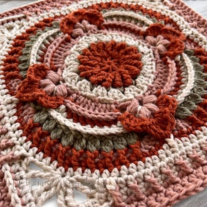 May include: A crocheted square with a circular design in the center. The design features multiple layers of crocheted circles in shades of brown, pink, and cream.