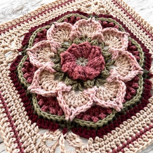 May include: A crocheted square featuring a floral design in shades of pink, green and burgundy. The centre of the square has a large flower with petals in a layered pattern.