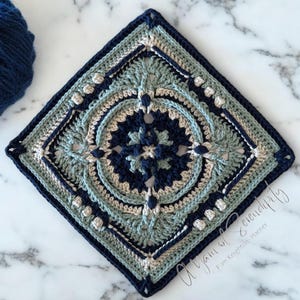 May include: A square crochet granny square with a detailed design in shades of blue, green, and beige. The square is made with a variety of stitches and textures, creating a visually interesting and intricate pattern. The text "A Yarn of Serenity" is visible in the bottom right corner of the image.
