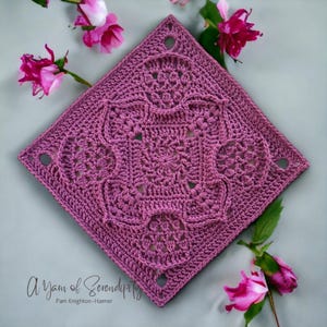 May include: A square crochet blanket in a deep pink color with a detailed pattern of interlocking circles and swirls. The blanket is surrounded by pink roses.