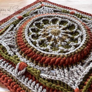 May include: A square, handmade crochet piece with a circular design in the center. The color palette includes shades of orange, green, gray, and brown. The piece has a textured appearance, with visible stitches and a detailed pattern. The text "A Yarn of Serenity" is visible.