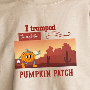 May include: Beige sweatshirt with a graphic that reads "I tromped through the PUMPKIN PATCH." The graphic features a cartoon pumpkin character in front of a desert landscape with cacti and mountains.