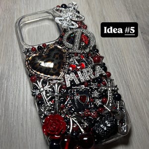 May include: Clear phone case embellished with red, black, and silver accents. Features a leopard print heart, a rose, and the word "Mira". The case is adorned with various charms and beads, and the text "Idea #5" is visible.