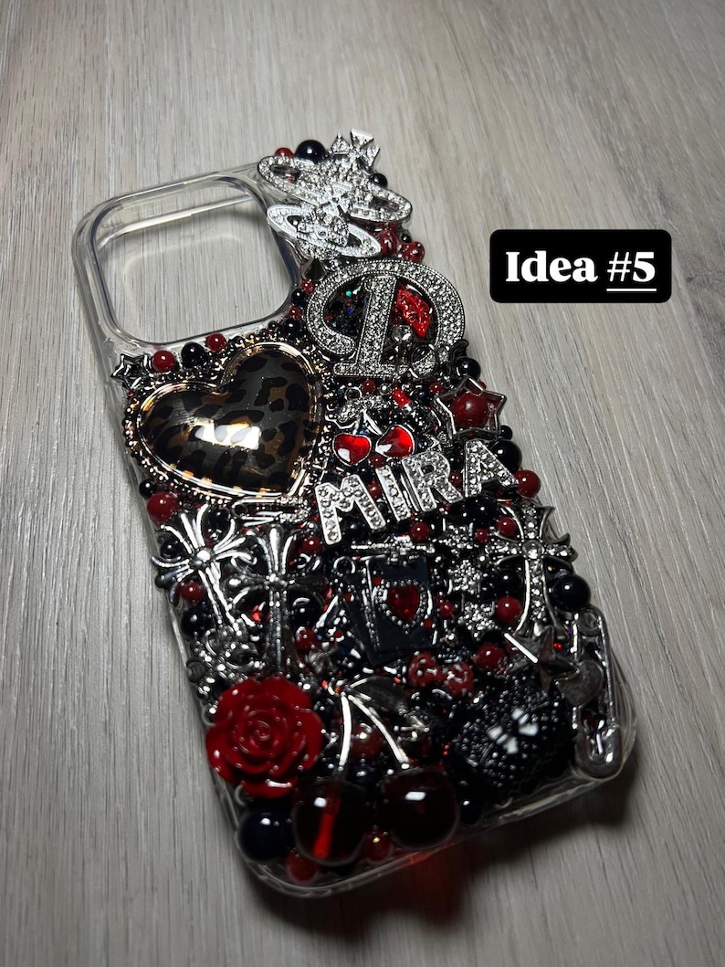 May include: Clear phone case embellished with red, black, and silver accents. Features a leopard print heart, a rose, and the word "Mira". The case is adorned with various charms and beads, and the text "Idea #5" is visible.