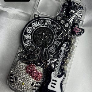 May include: Clear phone case with a variety of embellishments. Features a black and white guitar, a Hello Kitty design with pink glitter, a silver cross, and the text "Idea #7".