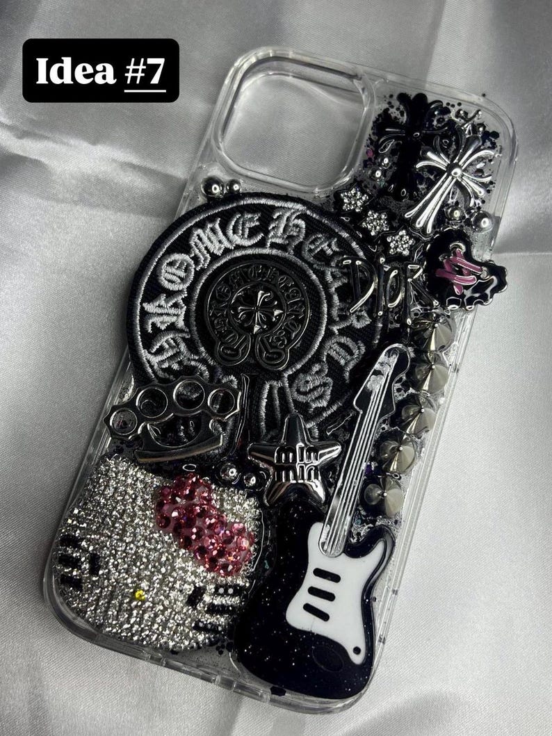 May include: Clear phone case with a variety of embellishments. Features a black and white guitar, a Hello Kitty design with pink glitter, a silver cross, and the text "Idea #7".