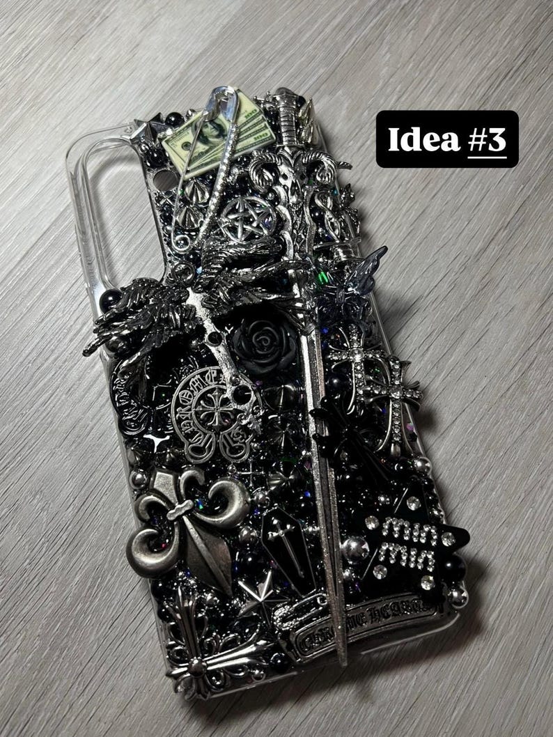 May include: A clear phone case heavily embellished with silver and black decorative elements, including crosses, fleur-de-lis, a rose, and a miniature sword. The text "Idea #3" is visible.
