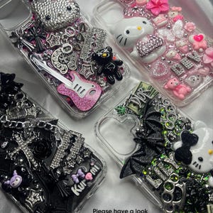 May include: Four clear phone cases with decorative embellishments. One case features a bedazzled Hello Kitty, another has a black teddy bear and a pink guitar. The third case has a black bat and a Hello Kitty. The fourth case has a black bow and the word "Kuromi".