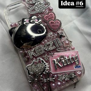 May include: Clear phone case with pink and silver embellishments. Features a silver Hello Kitty design, heart-shaped accents, and the word "KENZI" in rhinestones. Includes a pink "Kitty" credit card design and the text "Idea #6".