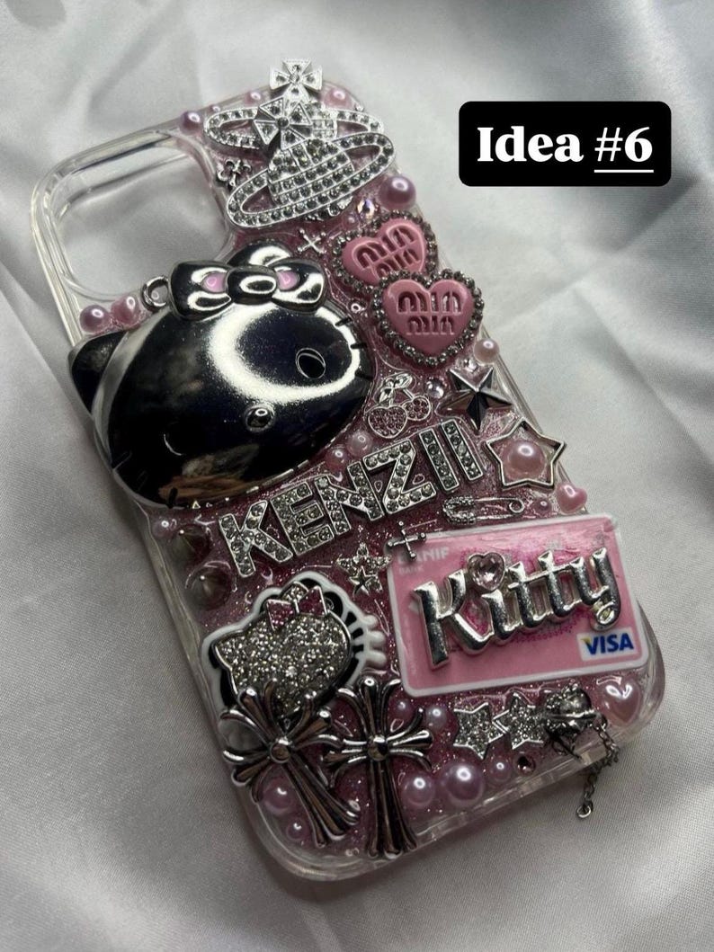 May include: Clear phone case with pink and silver embellishments. Features a silver Hello Kitty design, heart-shaped accents, and the word "KENZI" in rhinestones. Includes a pink "Kitty" credit card design and the text "Idea #6".