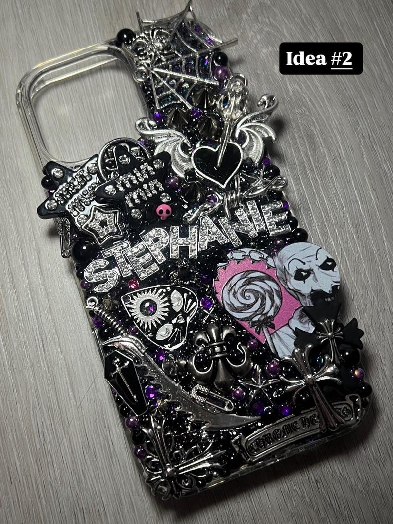 May include: A clear phone case heavily embellished with black and silver gothic-themed charms, including a spiderweb, hearts, and crosses. The name "STEPHANIE" is spelled out in silver rhinestones. The case also features a pink and white lollipop and a zombie-like illustration.