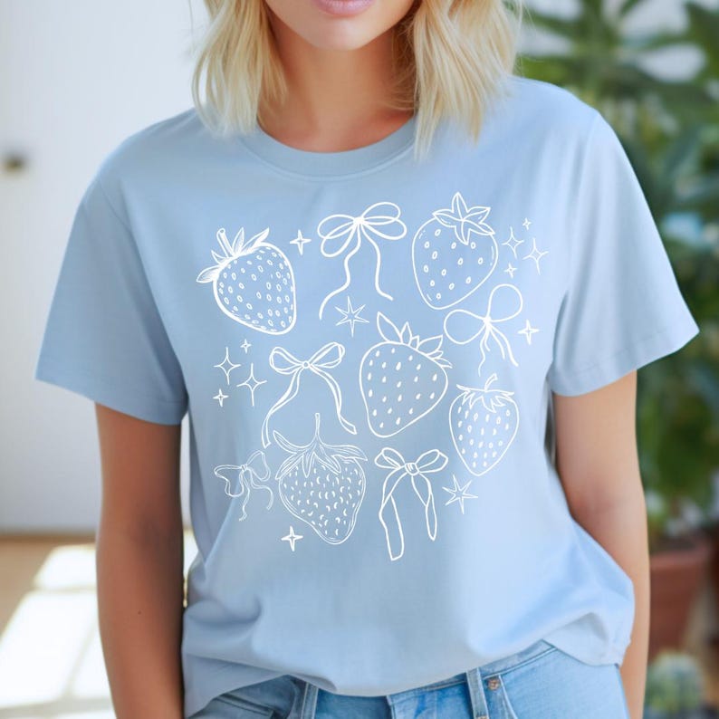 K&ouml;nnte beinhalten: Hellblaues T-Shirt mit einer wei&szlig;en Illustration von Erdbeeren, Schleifen und Sternen. Das Design ist auf einem weichen T-Shirt mit kurzen &Auml;rmeln aufgedruckt. Das Shirt hat einen Rundhalsausschnitt.