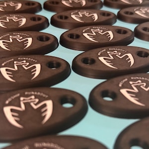 May include: A collection of oval-shaped, dark brown objects with a white graphic and text. Each object has two holes and the text "RUNABOUT" is visible. The objects are arranged on a light blue surface.