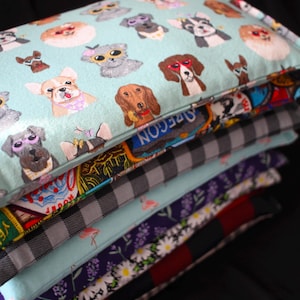 May include: A stack of six colorful fabric pillow covers with various patterns, including dogs wearing sunglasses, plaid, and floral designs.
