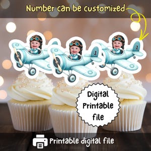 May include: Cupcakes topped with light blue airplane decorations featuring a baby wearing goggles. The text "Number can be customized" and "Digital Printable file" are also visible. The cupcakes have white frosting and pearl sprinkles.