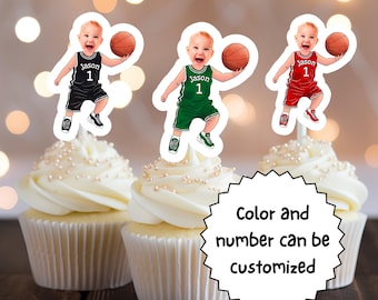 May include: Three cupcake toppers featuring a cartoon baby boy wearing a basketball uniform. The baby is holding a basketball and has a personalized name and number on the jersey. The jerseys are in black, green, and red.