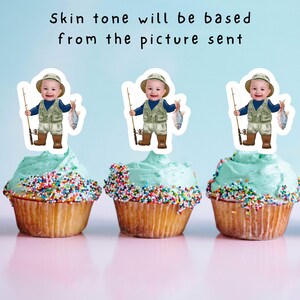 May include: Three cupcakes with blue frosting and colorful sprinkles topped with edible images of a boy dressed as a fisherman holding a fishing rod and a fish.