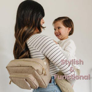 May include: A woman wearing a striped shirt is holding a toddler. She is wearing a beige quilted diaper bag with gold accents. The bag is worn as a hip pack. The text "Stylish & Functional" is superimposed on the image.